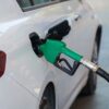 Close-up of a green nozzle refueling a white car at a gas station.
