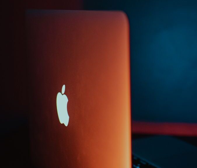 Minimalist laptop design featuring glowing Apple logo with dramatic lighting.