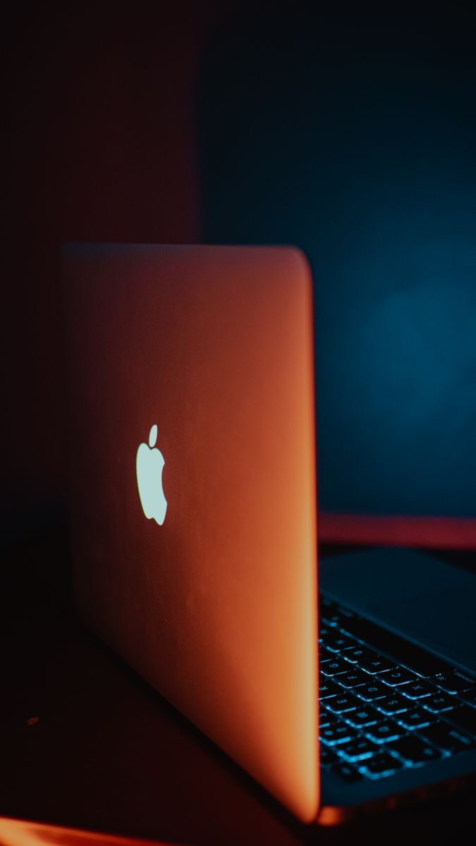 Minimalist laptop design featuring glowing Apple logo with dramatic lighting.