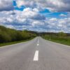 Open countryside road stretching into the horizon under a sky filled with dramatic clouds.