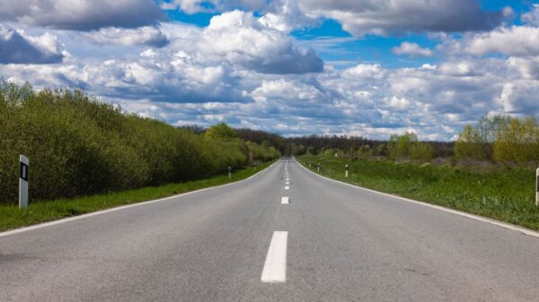 Open countryside road stretching into the horizon under a sky filled with dramatic clouds.