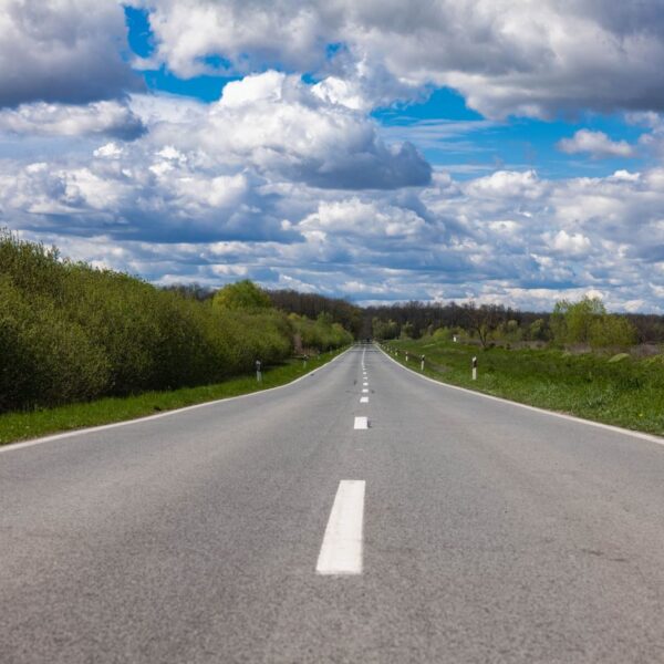 Open countryside road stretching into the horizon under a sky filled with dramatic clouds.