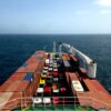 Aerial view of a cargo ship carrying containers and colorful vehicles on the open sea.
