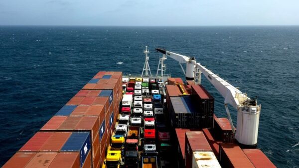 Aerial view of a cargo ship carrying containers and colorful vehicles on the open sea.