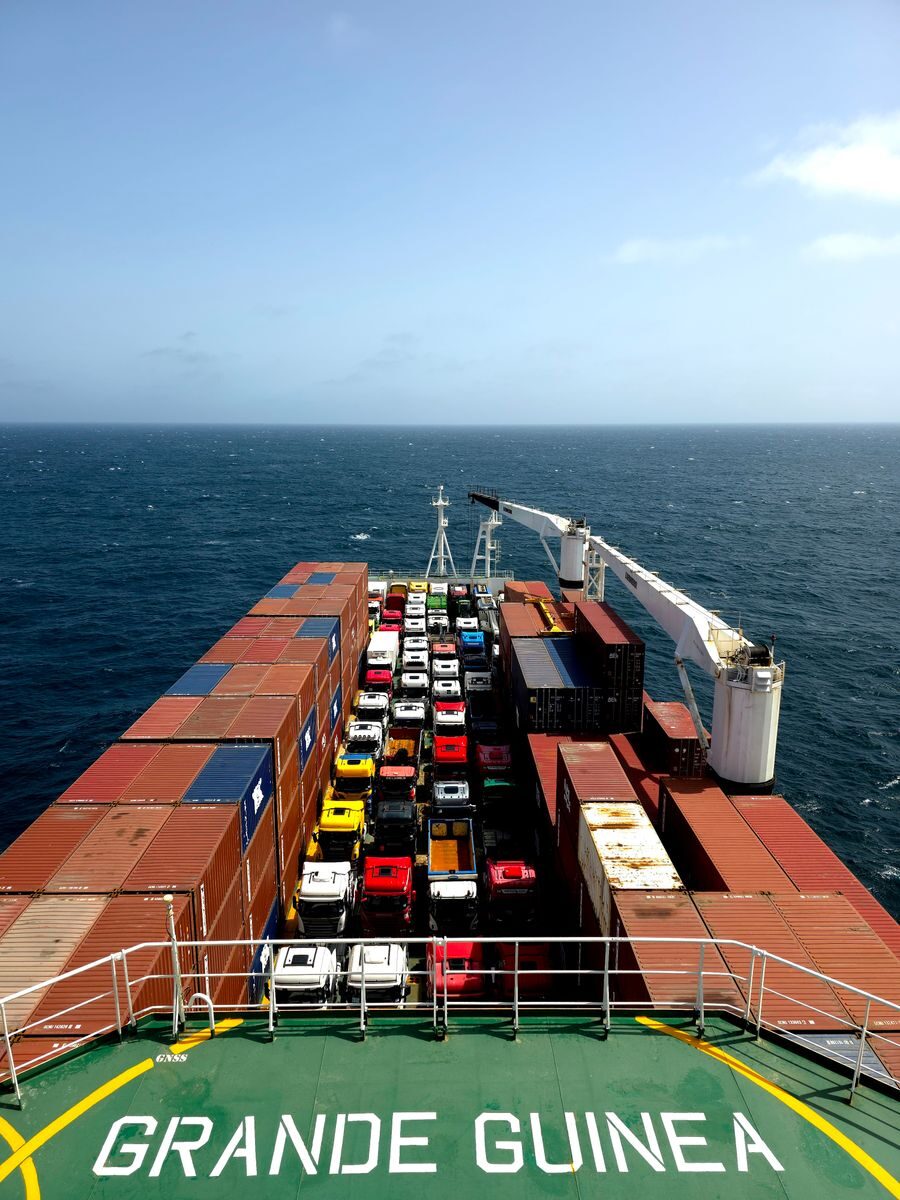 Aerial view of a cargo ship carrying containers and colorful vehicles on the open sea.