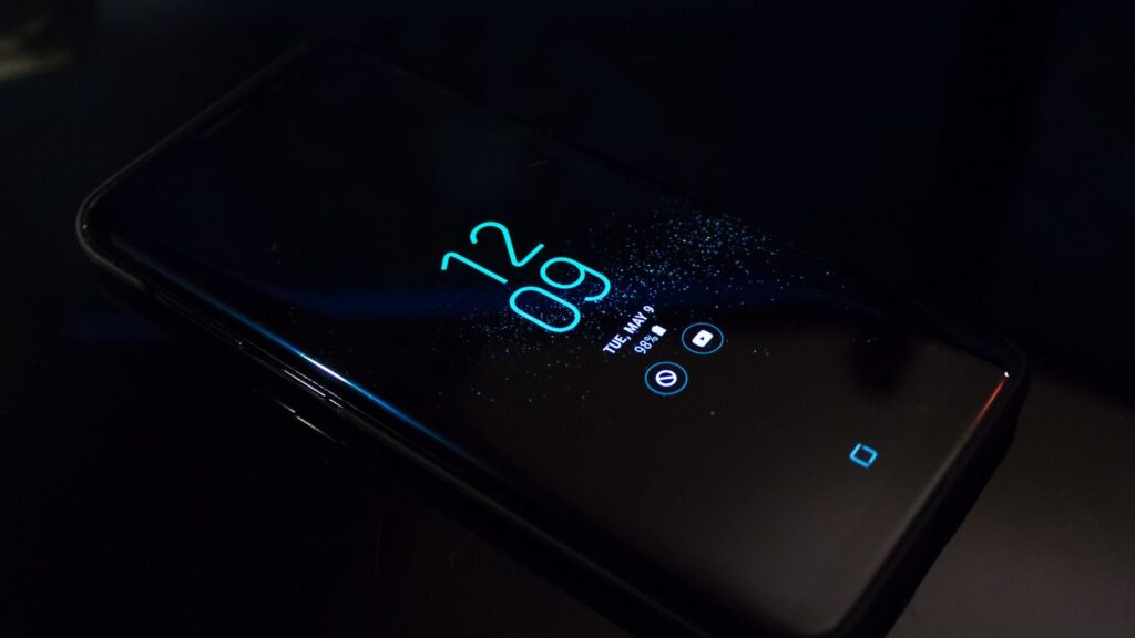 Close-up of a smartphone in the dark displaying digital clock and notifications.
