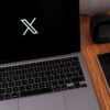 Minimalist desk setup featuring a laptop, smartphone, and clock on a wooden surface.