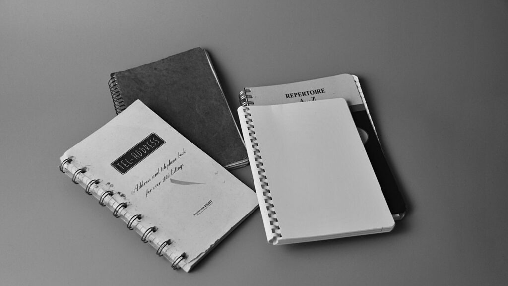 Black and white photo showing spiral notebooks with cover texts in a flat lay setup.