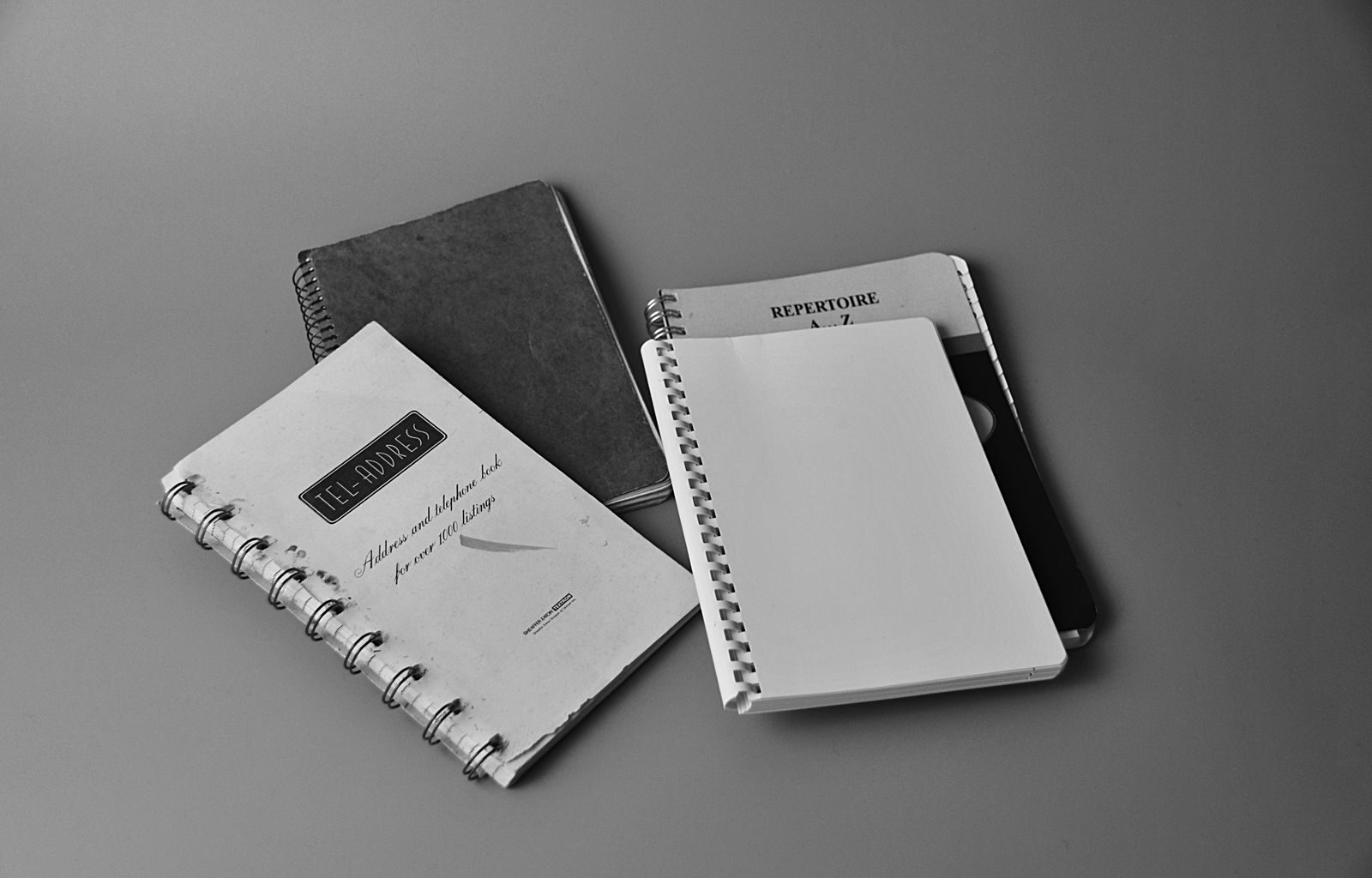 Black and white photo showing spiral notebooks with cover texts in a flat lay setup.