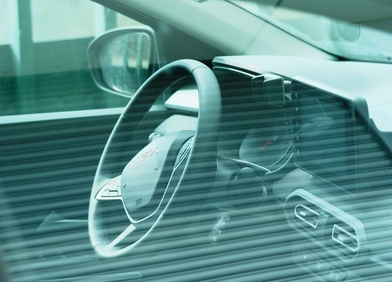 Close-up of a car's dashboard and steering wheel viewed through a tinted window.