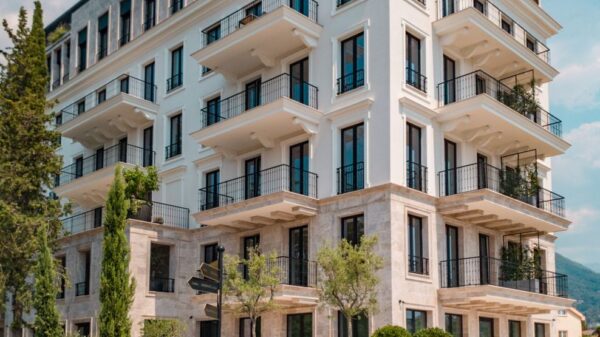 Elegant modern building with balconies and greenery in Tivat, Montenegro, under a clear blue sky.
