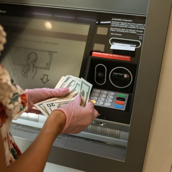 A person wearing gloves withdraws cash from an ATM, ensuring hygiene.