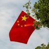 Vibrant Chinese flag waves amongst green foliage under the expansive sky.