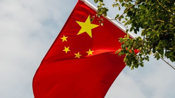 Vibrant Chinese flag waves amongst green foliage under the expansive sky.