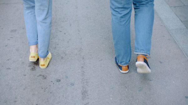 Two people walking casually on a city pavement in jeans and sneakers.
