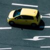 Aerial view of a yellow car on a road with directional arrows, highlighting urban transport.