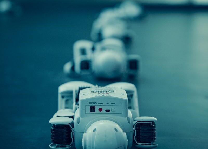 Vertical shot of white robots aligned on a dark surface, emphasizing technology.