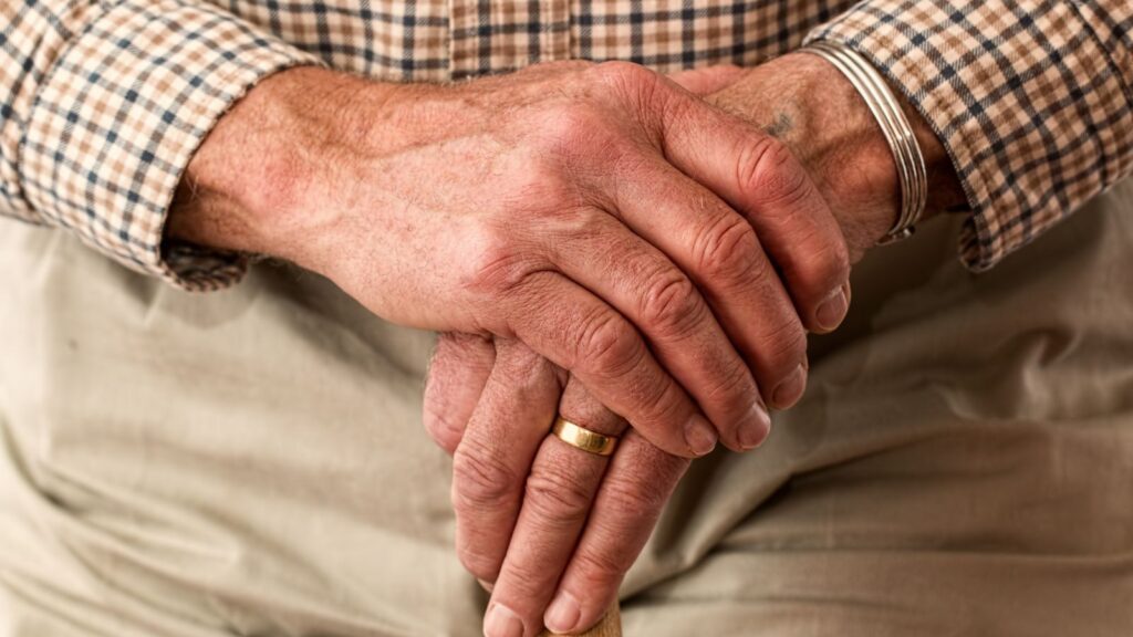 A detailed image of elderly hands clasping a wooden cane, symbolizing aging and support.