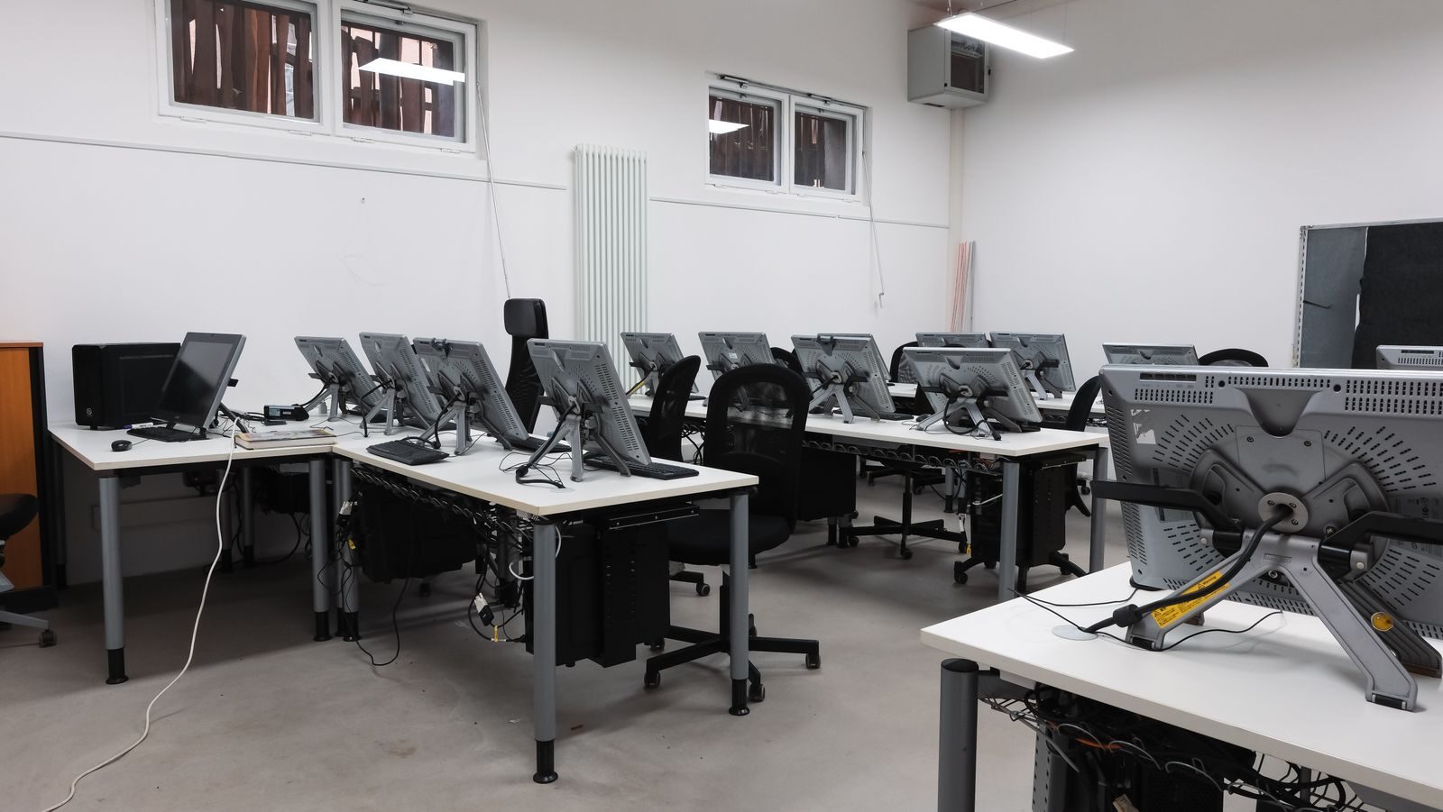 An empty computer lab featuring multiple vacant workstations with modern monitors.