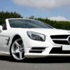 Stunning white Mercedes Benz convertible parked on the road against a lush green backdrop.