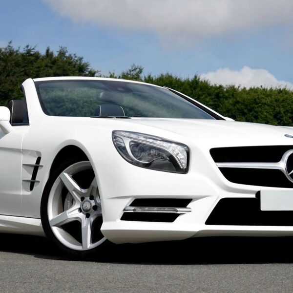 Stunning white Mercedes Benz convertible parked on the road against a lush green backdrop.