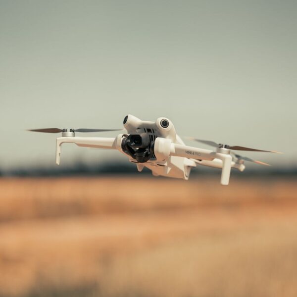White drone flying over a golden field on a clear day, showcasing modern technology.