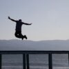 Dramatic silhouette capture of a man leaping over a pier with lake and mountains in the background in İznik, Türkiye.