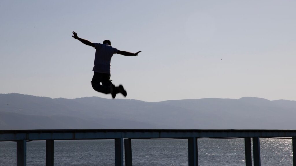 Dramatic silhouette capture of a man leaping over a pier with lake and mountains in the background in İznik, Türkiye.