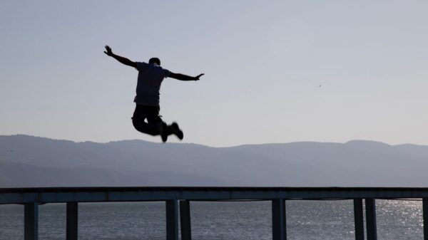 Dramatic silhouette capture of a man leaping over a pier with lake and mountains in the background in İznik, Türkiye.