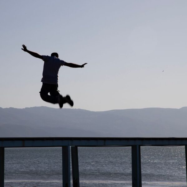 Dramatic silhouette capture of a man leaping over a pier with lake and mountains in the background in İznik, Türkiye.