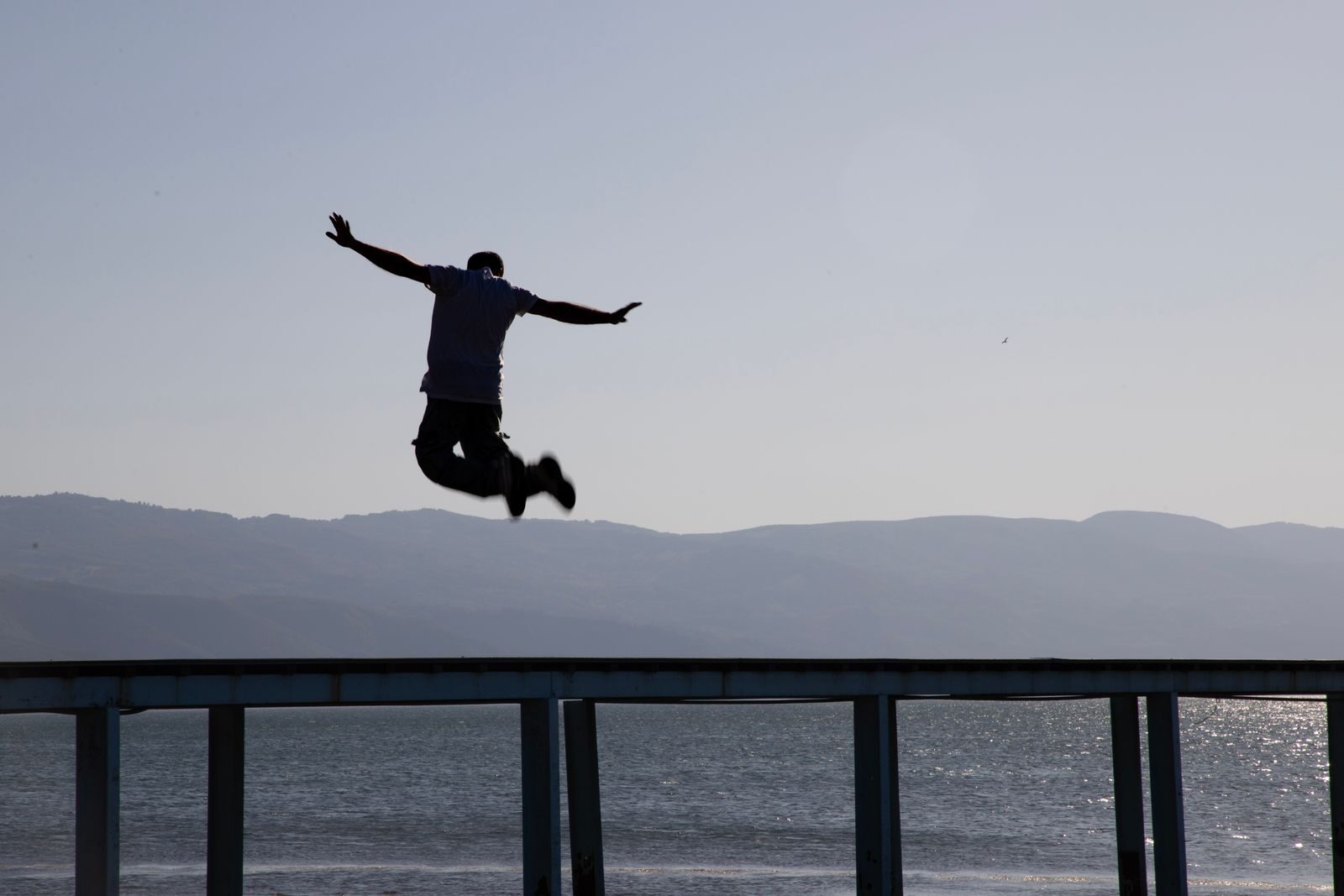 Dramatic silhouette capture of a man leaping over a pier with lake and mountains in the background in İznik, Türkiye.