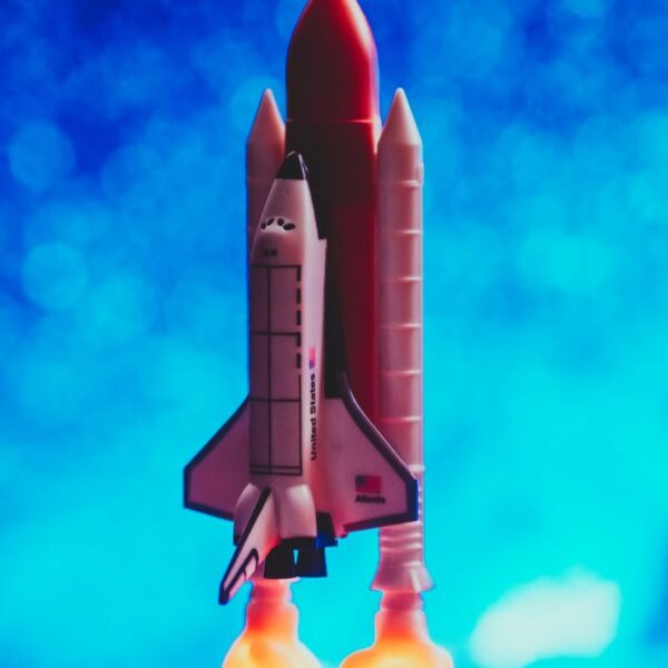 A toy rocket ship launching with vibrant flames against a bright blue bokeh background.