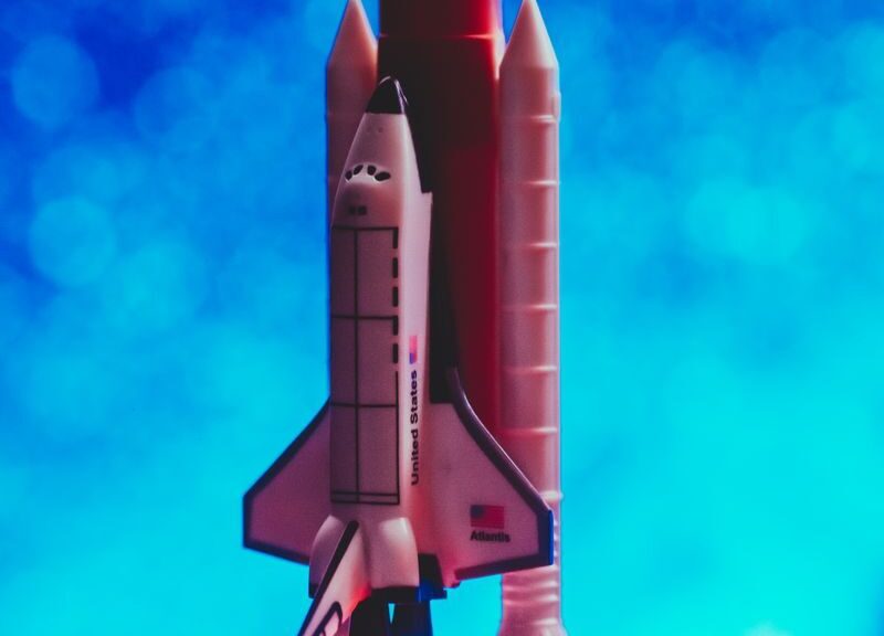 A toy rocket ship launching with vibrant flames against a bright blue bokeh background.