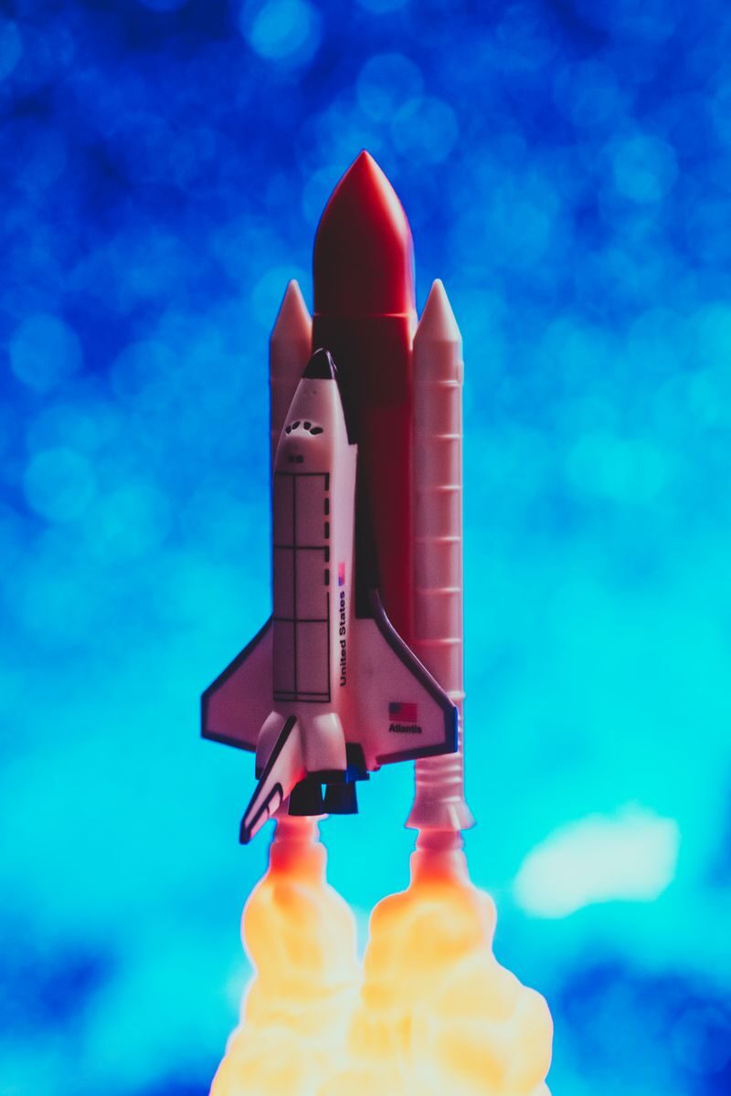 A toy rocket ship launching with vibrant flames against a bright blue bokeh background.