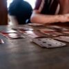 Intimate tabletop scene of people playing cards with a focus on hands and playing cards.