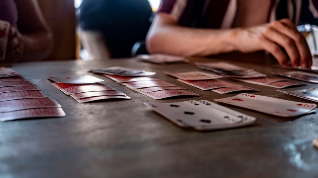 Intimate tabletop scene of people playing cards with a focus on hands and playing cards.