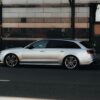 A silver luxury car parked on a Berlin street with modern architecture reflecting in city windows.