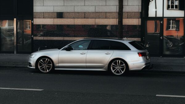 A silver luxury car parked on a Berlin street with modern architecture reflecting in city windows.