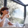 Thoughtful woman with glasses and short hair looking out window in a modern room.