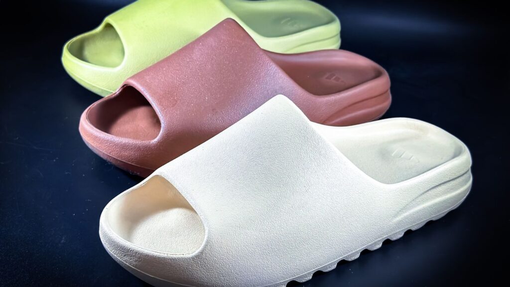 Close-up of a variety of stylish slides in earth tones on a dark background, emphasizing modern footwear design.