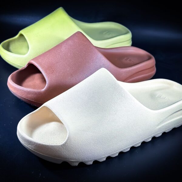 Close-up of a variety of stylish slides in earth tones on a dark background, emphasizing modern footwear design.