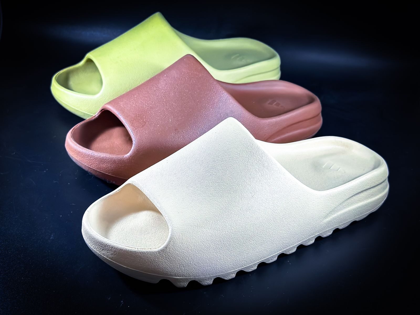 Close-up of a variety of stylish slides in earth tones on a dark background, emphasizing modern footwear design.