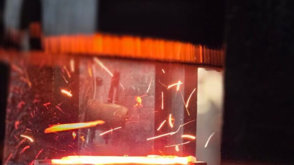 Close-up of glowing metal being forged, with bright sparks flying, capturing the industrial process.