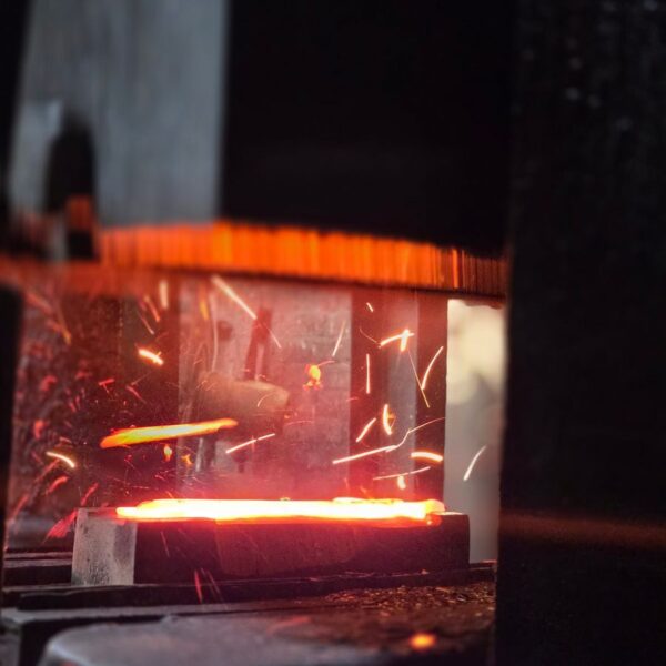 Close-up of glowing metal being forged, with bright sparks flying, capturing the industrial process.