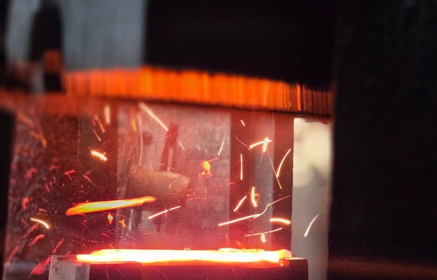 Close-up of glowing metal being forged, with bright sparks flying, capturing the industrial process.