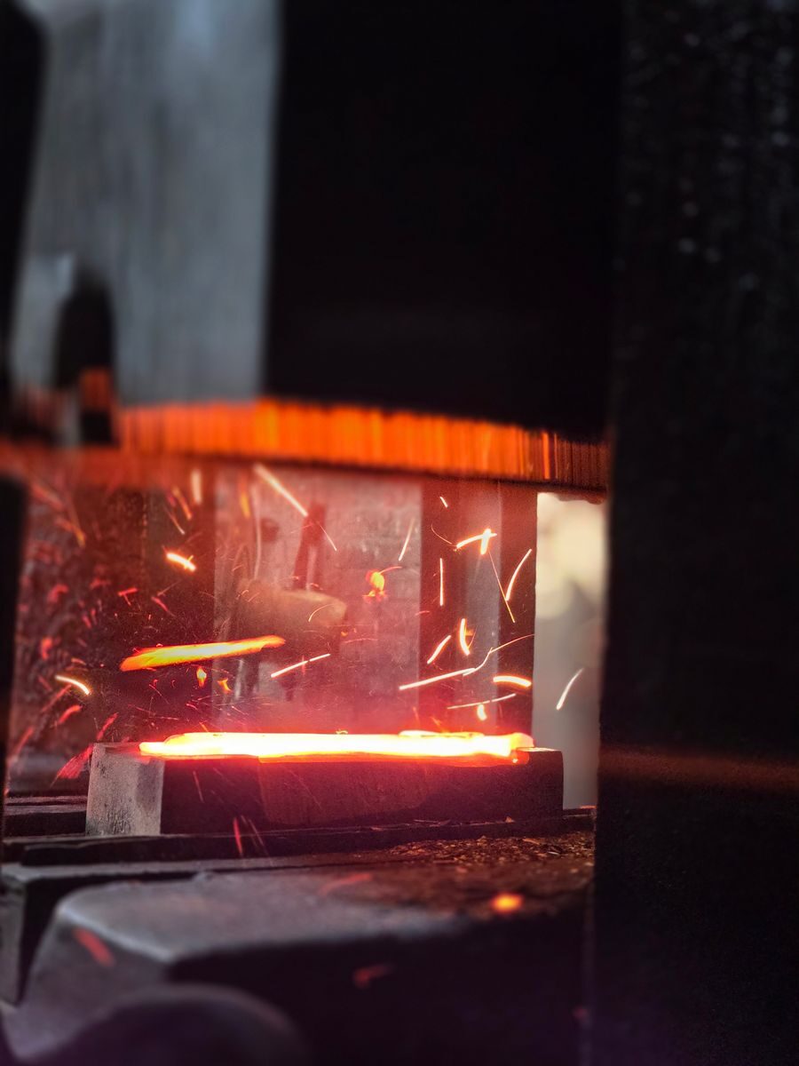 Close-up of glowing metal being forged, with bright sparks flying, capturing the industrial process.