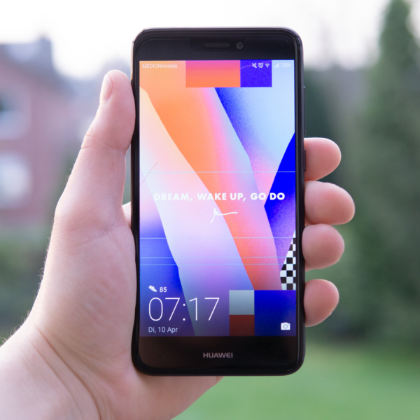 Hand holding a Huawei smartphone displaying a colorful screen outdoors in Germany.
