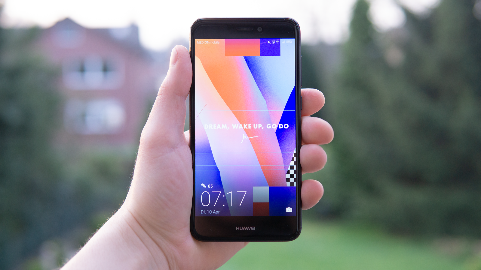 Hand holding a Huawei smartphone displaying a colorful screen outdoors in Germany.