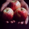Close-up of hands gently holding three ripe red apples, perfect for healthy eating.
