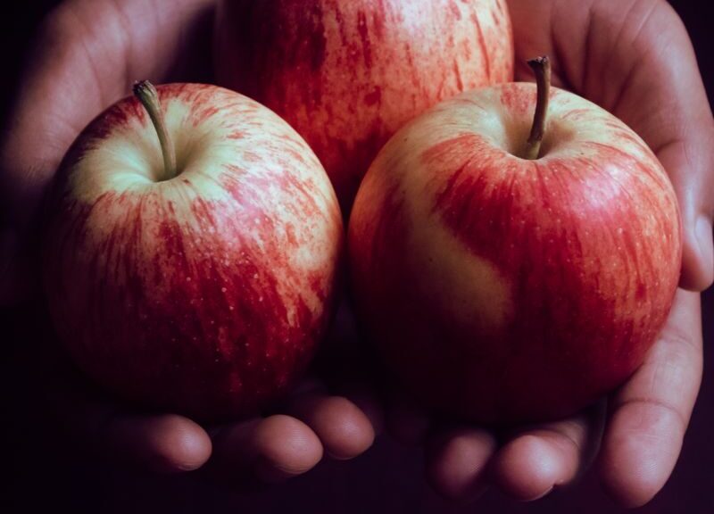 Close-up of hands gently holding three ripe red apples, perfect for healthy eating.